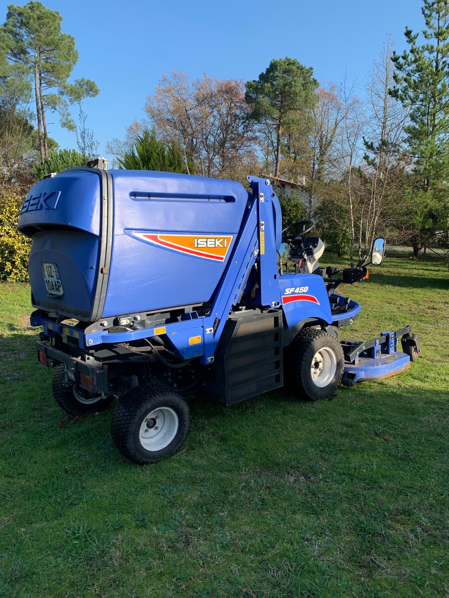 Tondeuse professionnelle Iseki SF450 bleue avec grand bac de ramassage, immatriculation DZ-104-AP, sur pelouse verte.